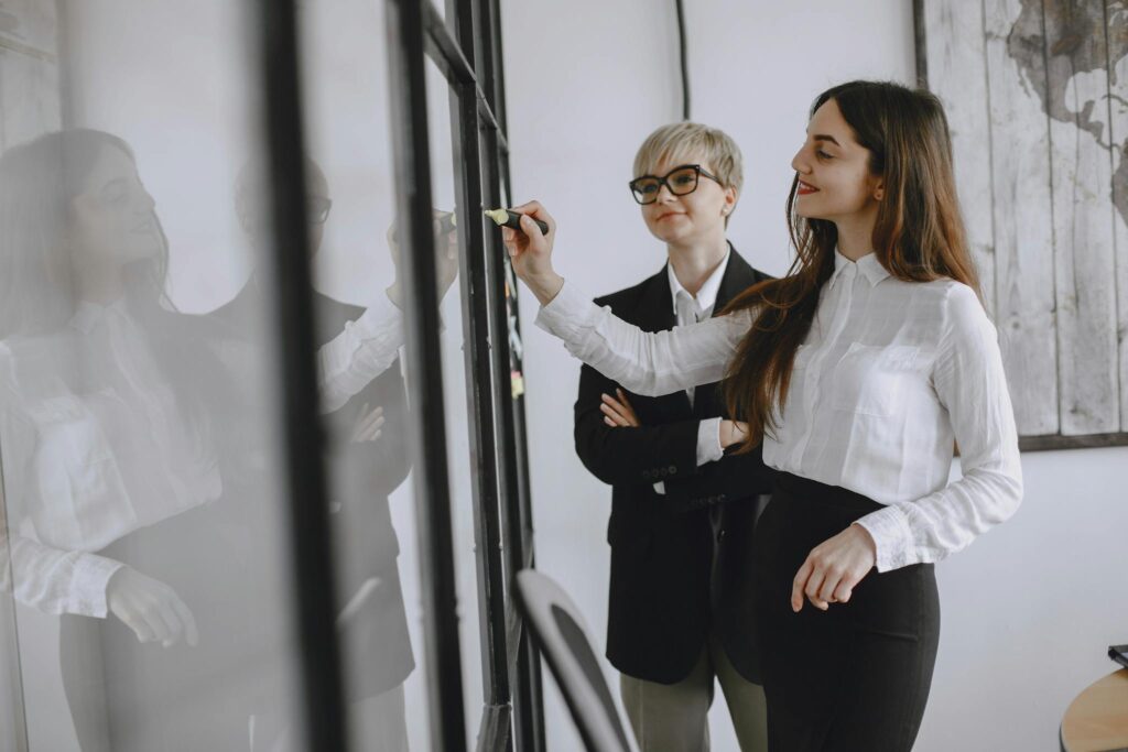 Two professional women collaborating in a modern office setting, focusing on teamwork and strategy.
